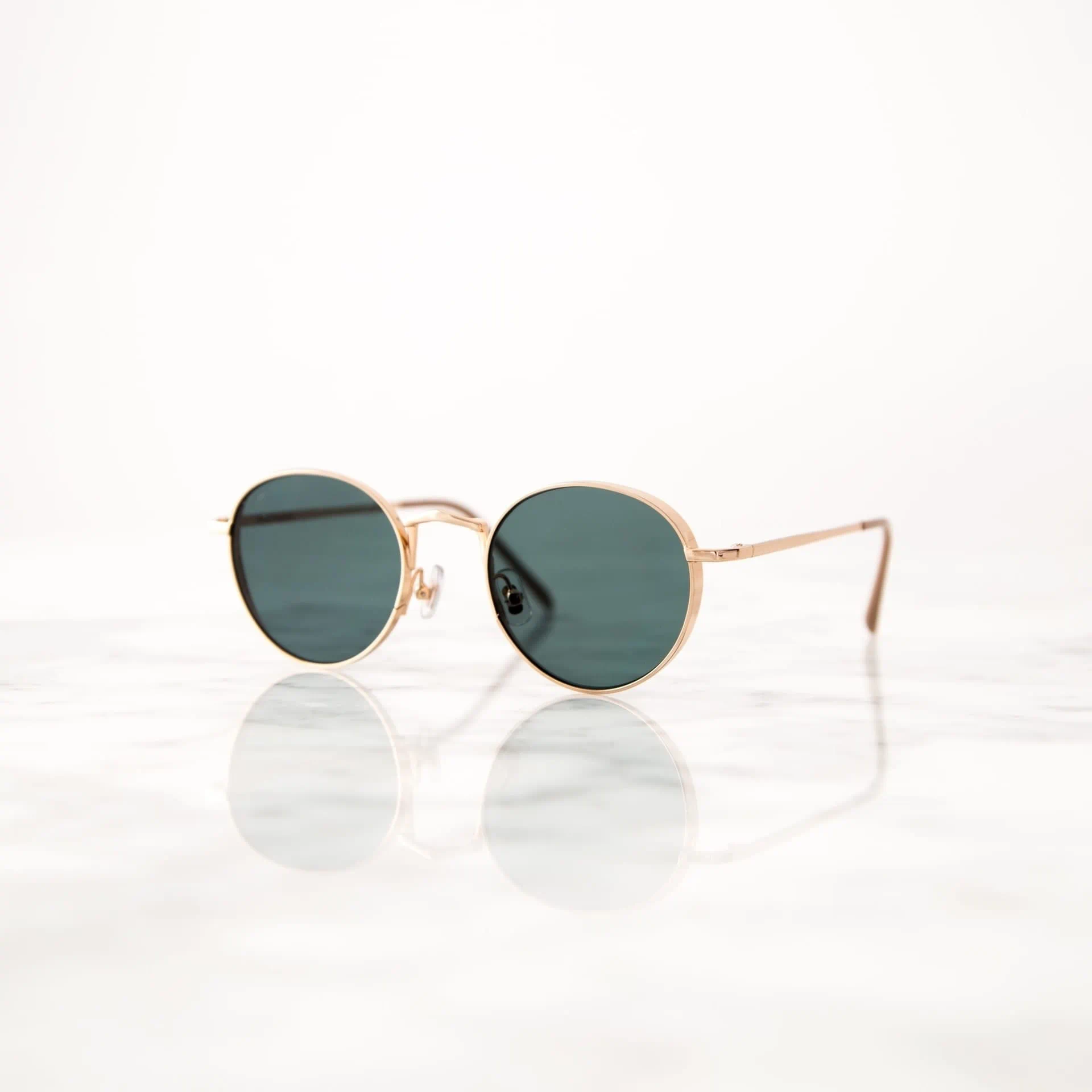 Sonnenbrille mit goldenem Gestell auf reflektierendem Marmoruntergrund